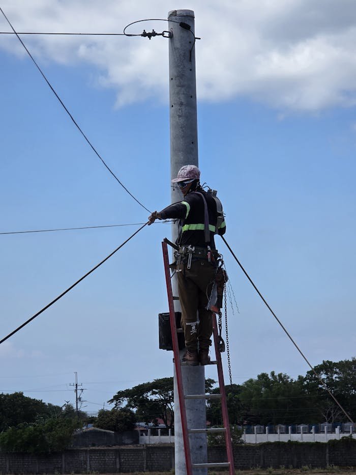 Electrician on ladder fixing overhead power lines. Outdoors in daylight.